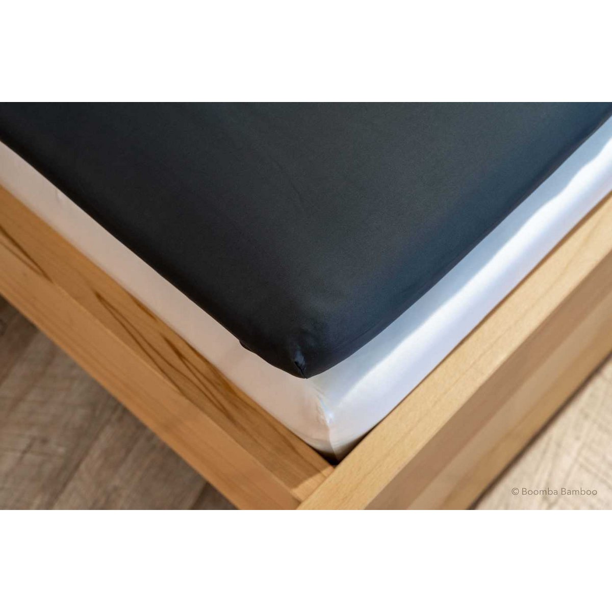 Space Blue bamboo fitted sheet for mattress toppers, showing its deep pocket fitted over a topper corner on a wood bed frame.