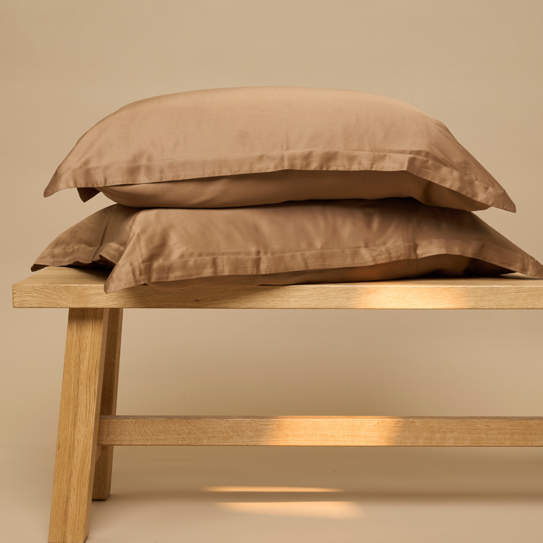 Stacked Eco Bamboo pillowcases in Hazel on a wooden bench