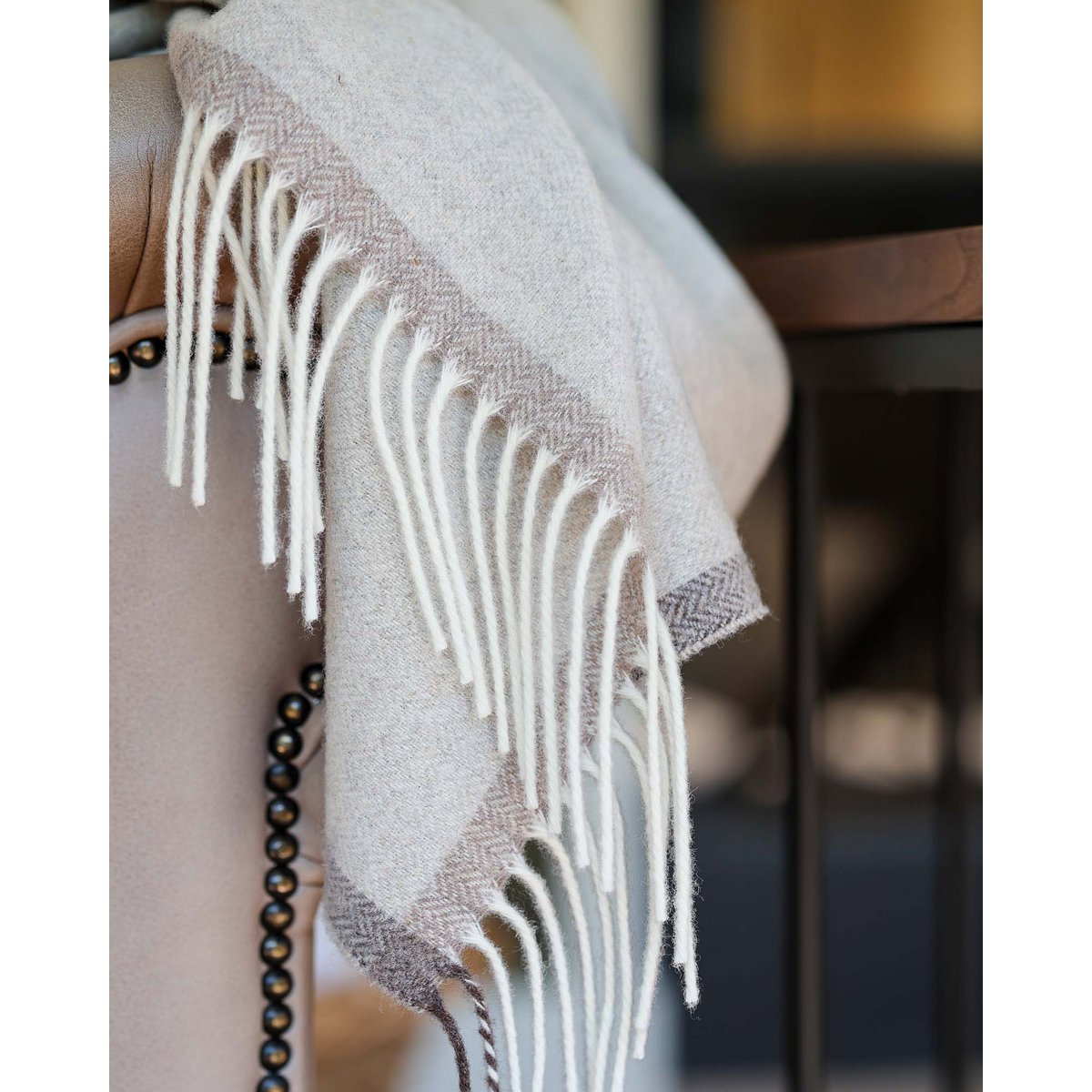 Das Plaid Milano in Beige mit langen Fransen, über die Armlehne eines Sofas drapiert