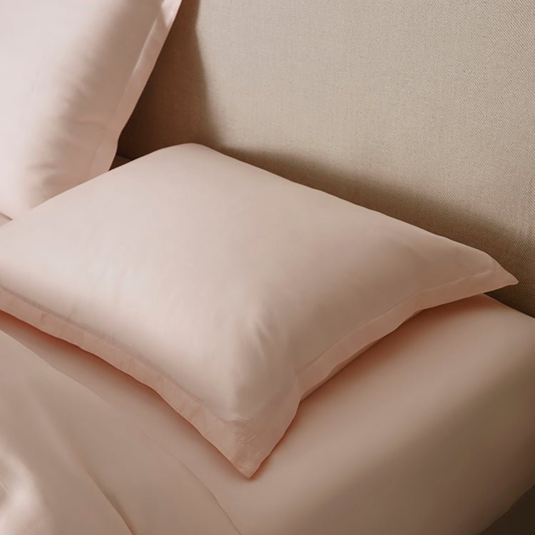 Tencel™ Sateen Pillowcase in Peach White styled on a bed against an upholstered headboard