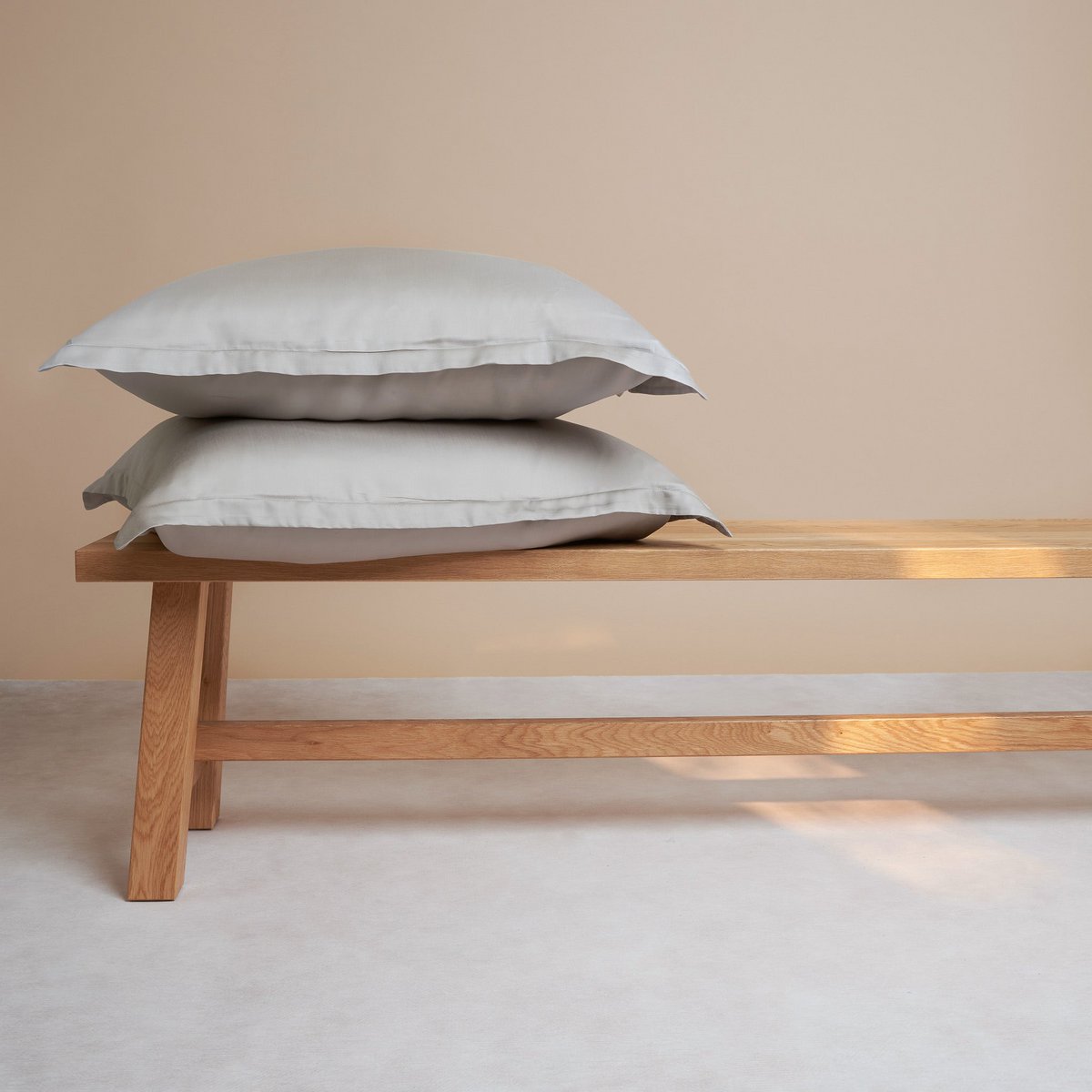 Tencel™ Sateen Pillowcases in Taupe, stacked on a wooden bench