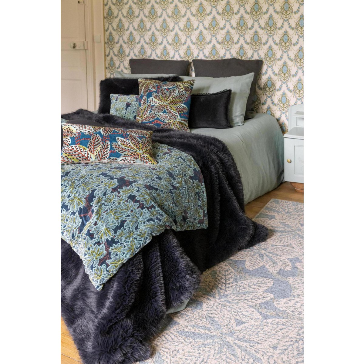Een Nolan-plaid in diepzwart, gedrapeerd over een bed met beddengoed met een patroon