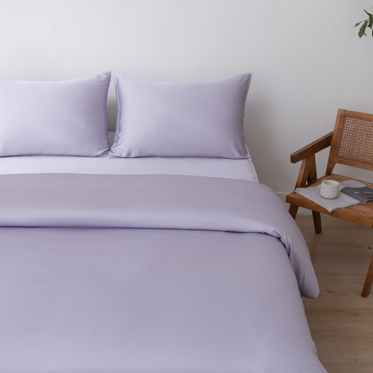 Bamboo duvet cover in Lavender Mist on a bed beside a cane chair with a cup and book
