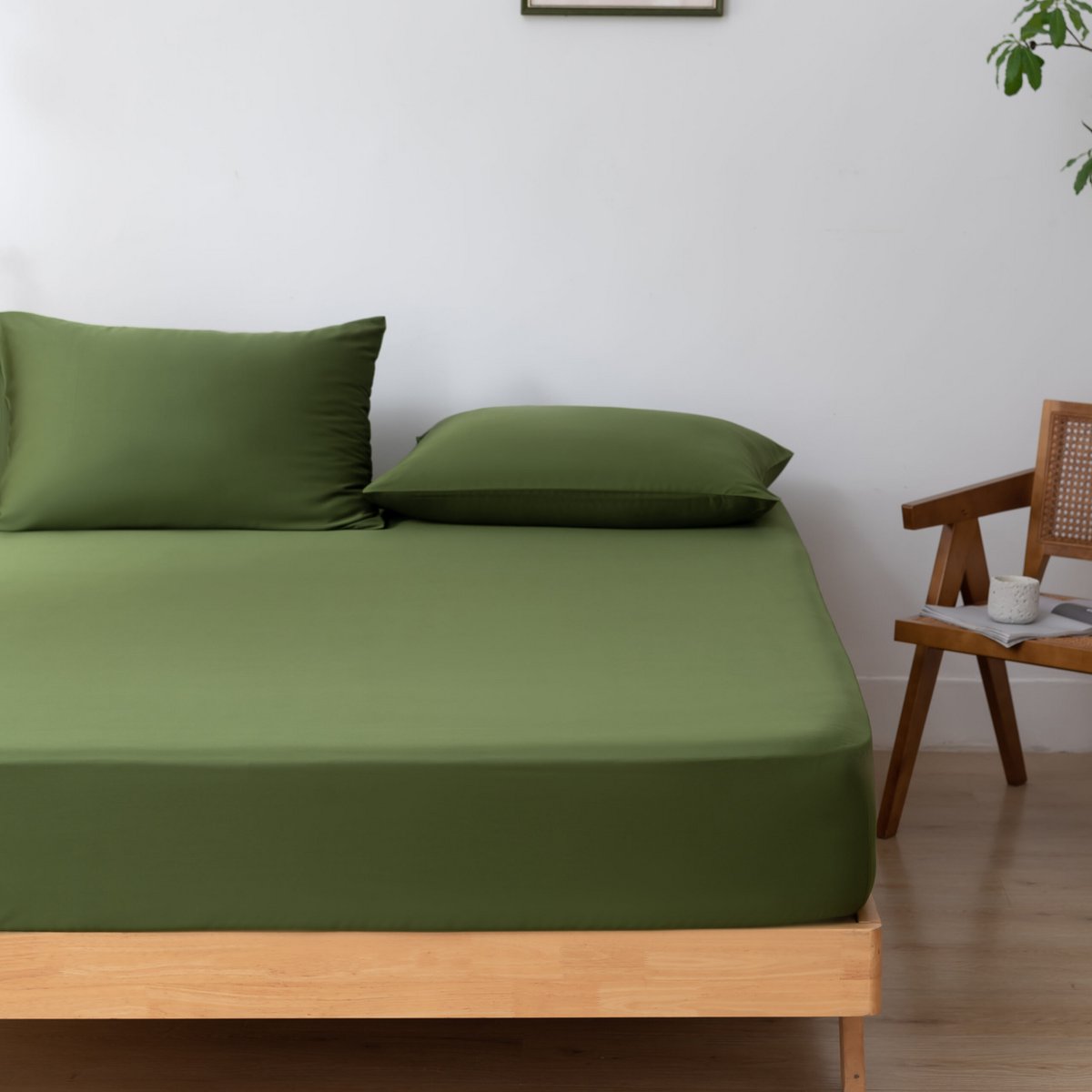 Deep Moss bamboo fitted sheet on a bed beside a cane chair with a cup and notebook.