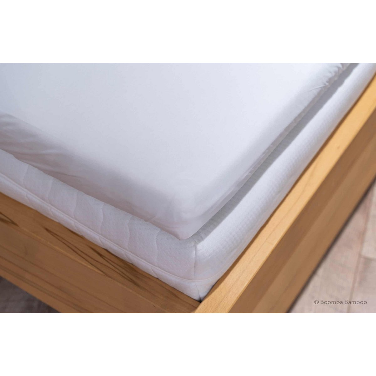 Coco White bamboo fitted sheet for mattress toppers, showing its deep pocket fitted over a topper corner on a wood bed frame.