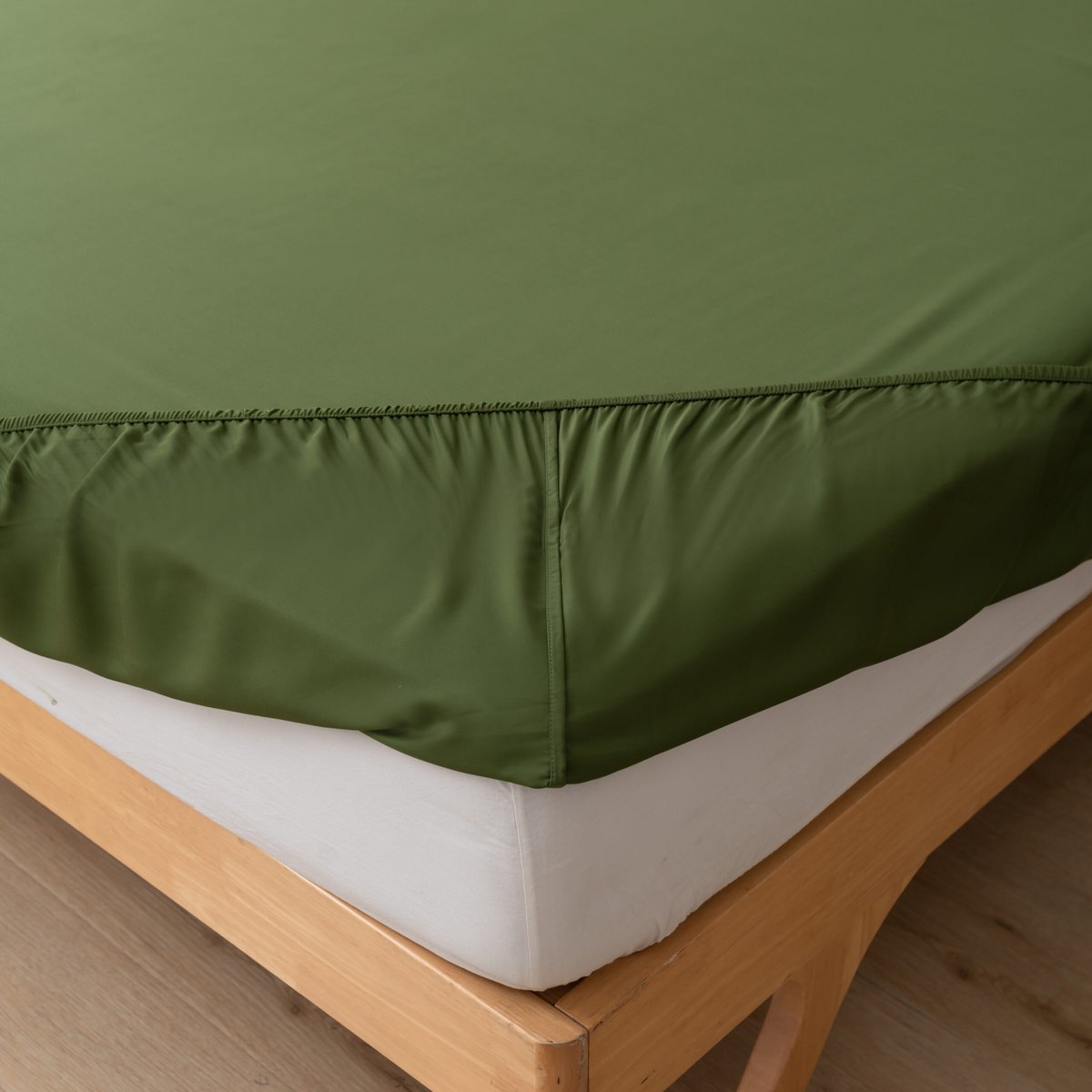 Close-up of the Deep Moss bamboo fitted sheet's corner fitted over a mattress on a wood bed frame.