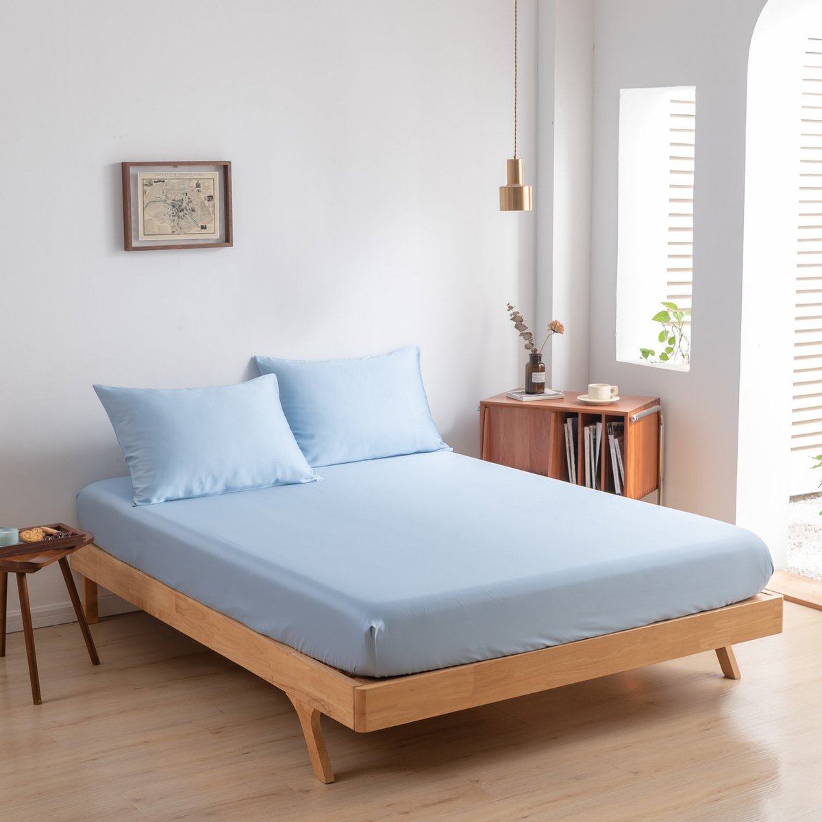 Sky Blue bamboo fitted sheet styled on a wood-frame bed by a window, with matching pillowcases.