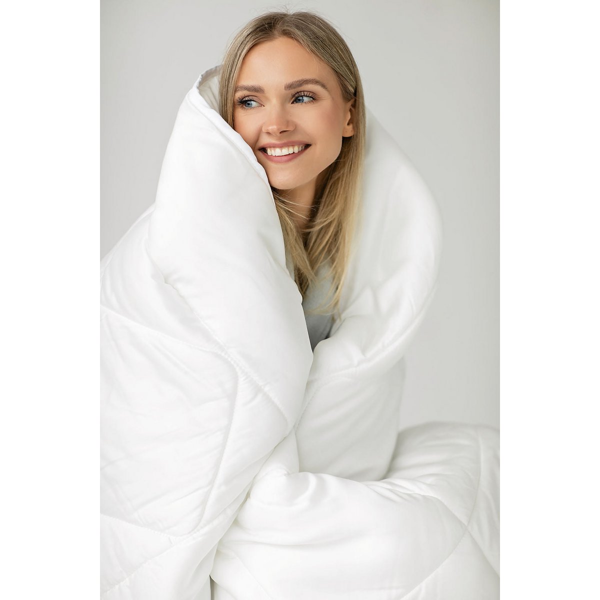 Woman smiling while wrapped in the white Super Soft Mono Tencel satin duvet