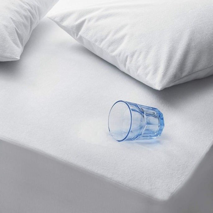 A blue glass of water tipped over on the white terry mattress protector, demonstrating its waterproof surface
