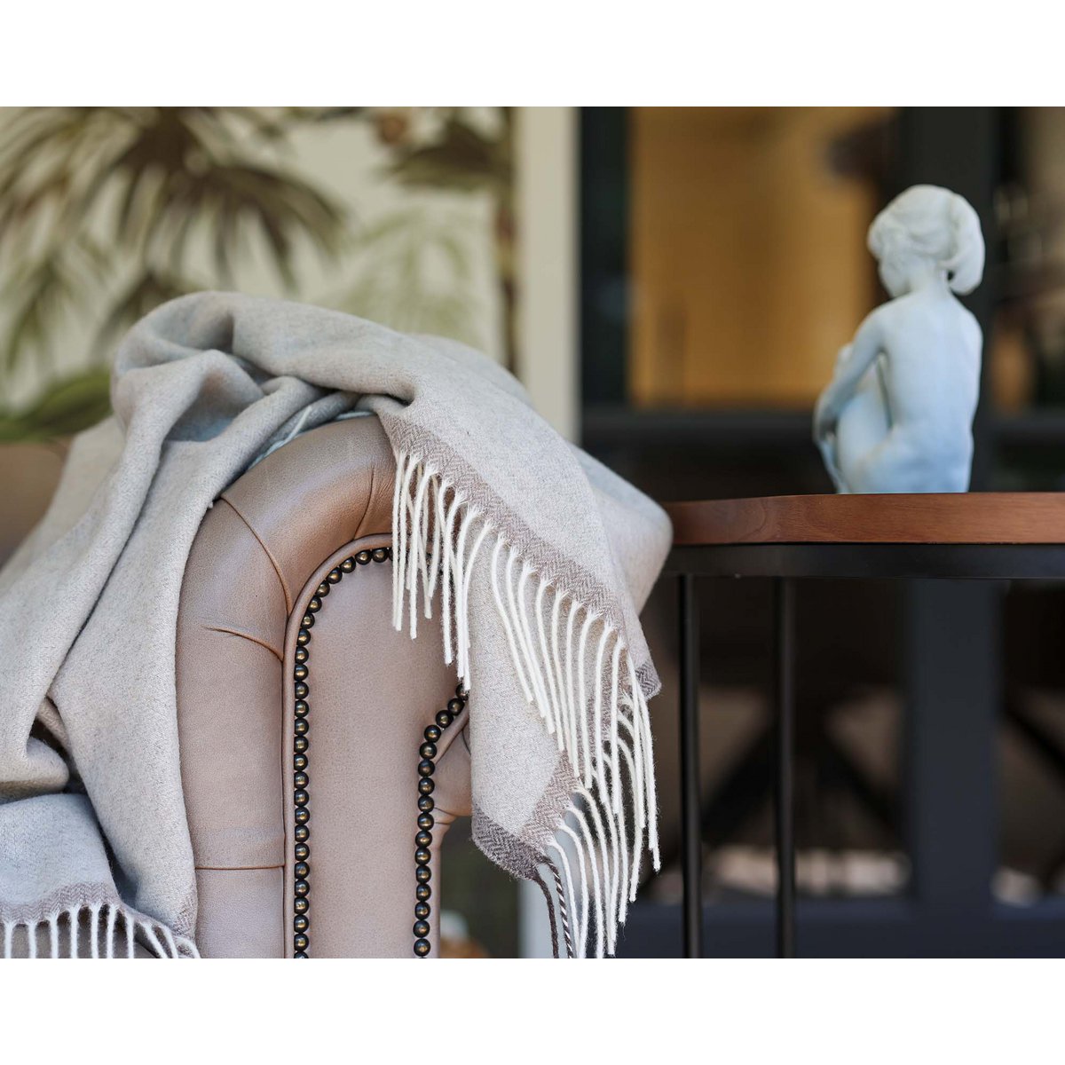 Das beige Milano-Plaid, das über die Armlehne eines Ledersofas drapiert ist