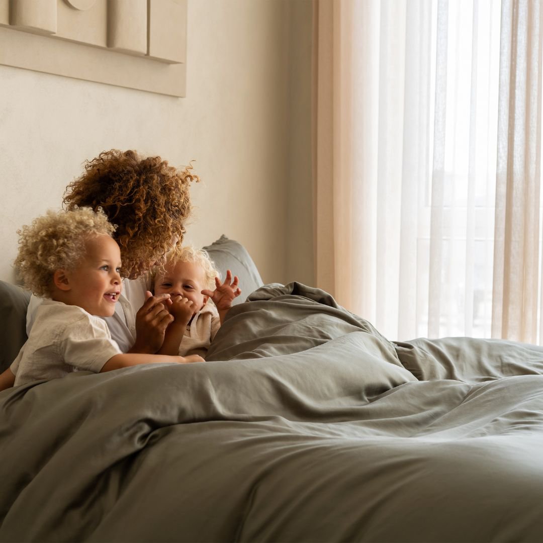 Parent and child relaxing on a bed dressed in the Tencel™ Twill Duvet Cover in Olive Green
