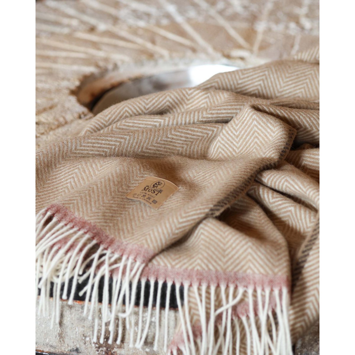 Gros plan sur le plaid de Denver en laine couleur camel à motif chevrons, orné d'une bande rose sur les bords et de franges
